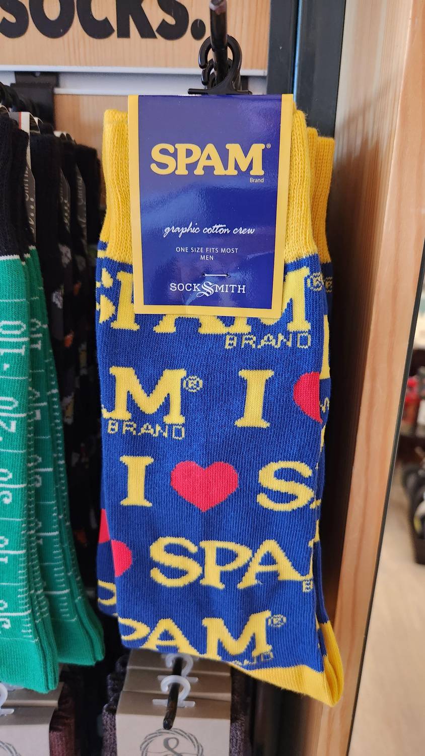 A pair of blue and yellow socks on a store display hook, printed all over with I heart SPAM and the SPAM logo.