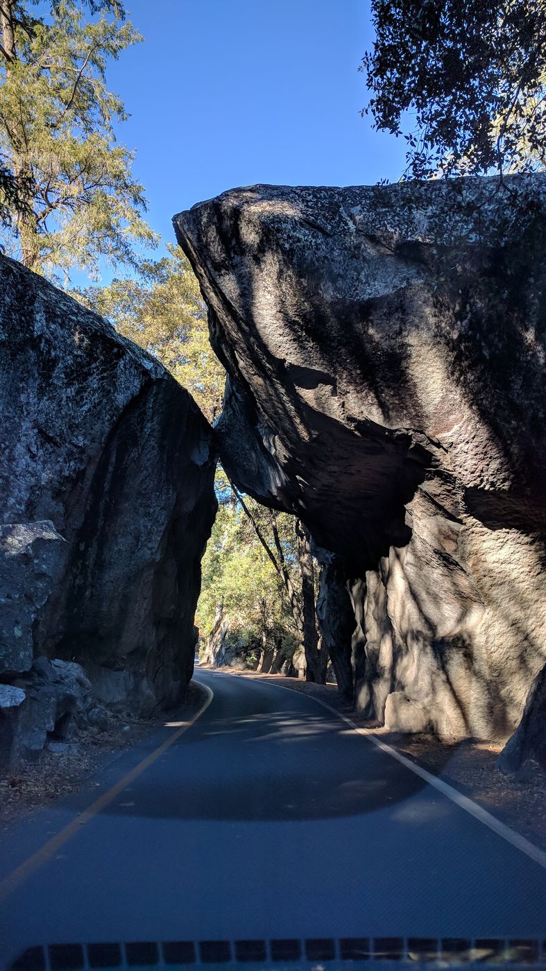 A two-lane road passing under two huge leaning granite boulders at the Arch Rock entrance to Yosemite.