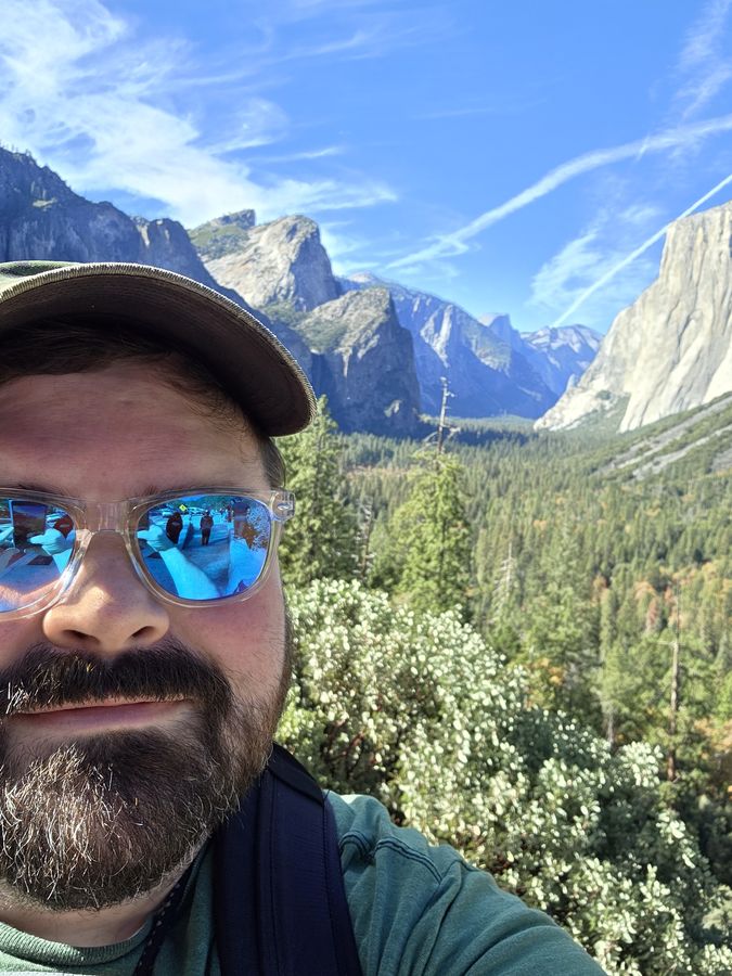 Joe Graham in a cap and mirrored sunglasses smiling in front of Tunnel View.