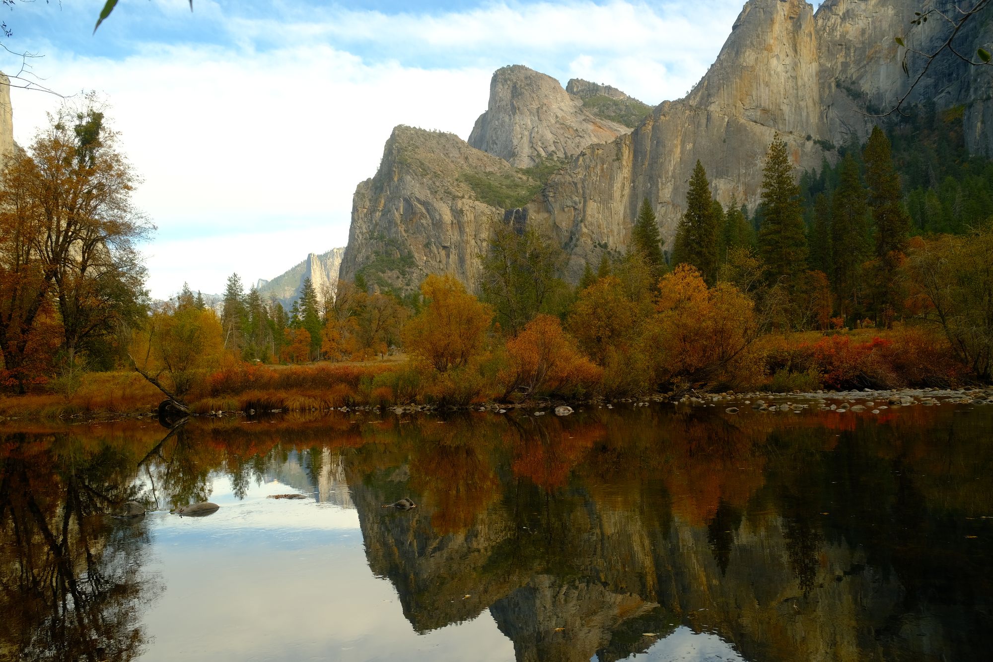 The Merced River lying perfectly still, reflecting granite spires, pines, and orange autumn trees at Valley View in Yosemite.