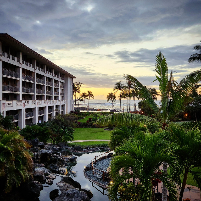 Tropical resort landscape at the Fairmont Orchid on Hawaii Island during blue hour, with palms, volcanic rock, water, and warm sunset color.