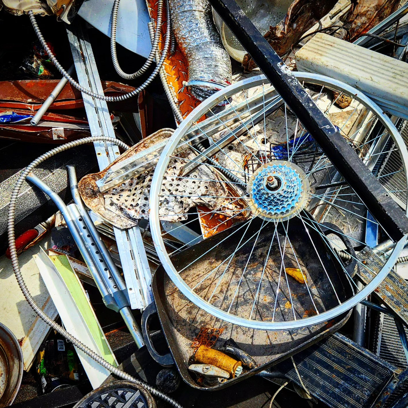 A dense pile of mixed scrap metal, including a bicycle wheel, a frying pan, conduit, and wire, at a recycling yard in North Birmingham, Alabama.