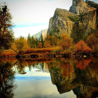 Perfect reflection of Yosemite Valley granite cliffs in still Merced River water with autumn foliage, California